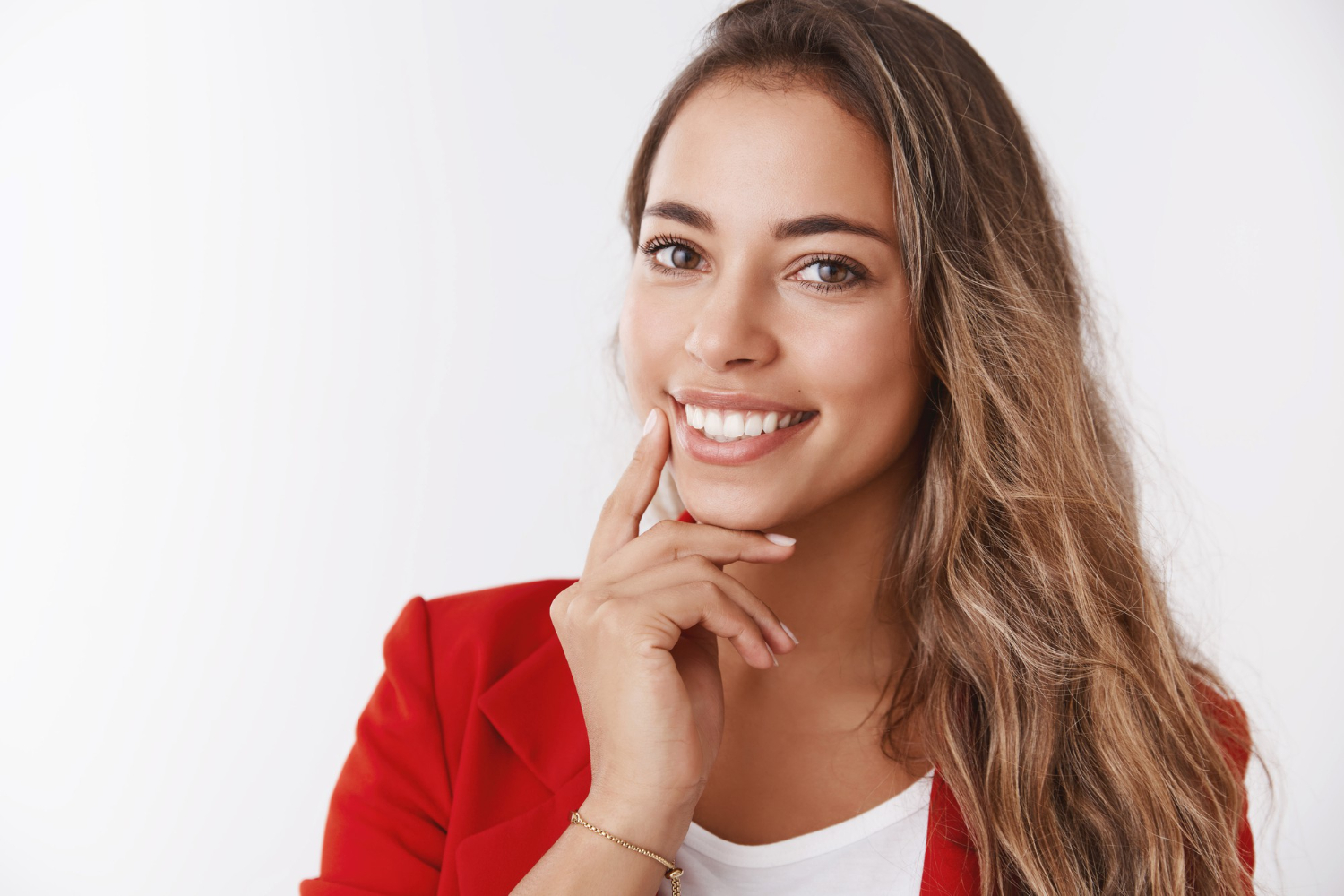 Mulher sorridente de blazer vermelho aponta para o sorriso saudável em tratamento de retração gengival na Myai Odontologia no Aricanduva.