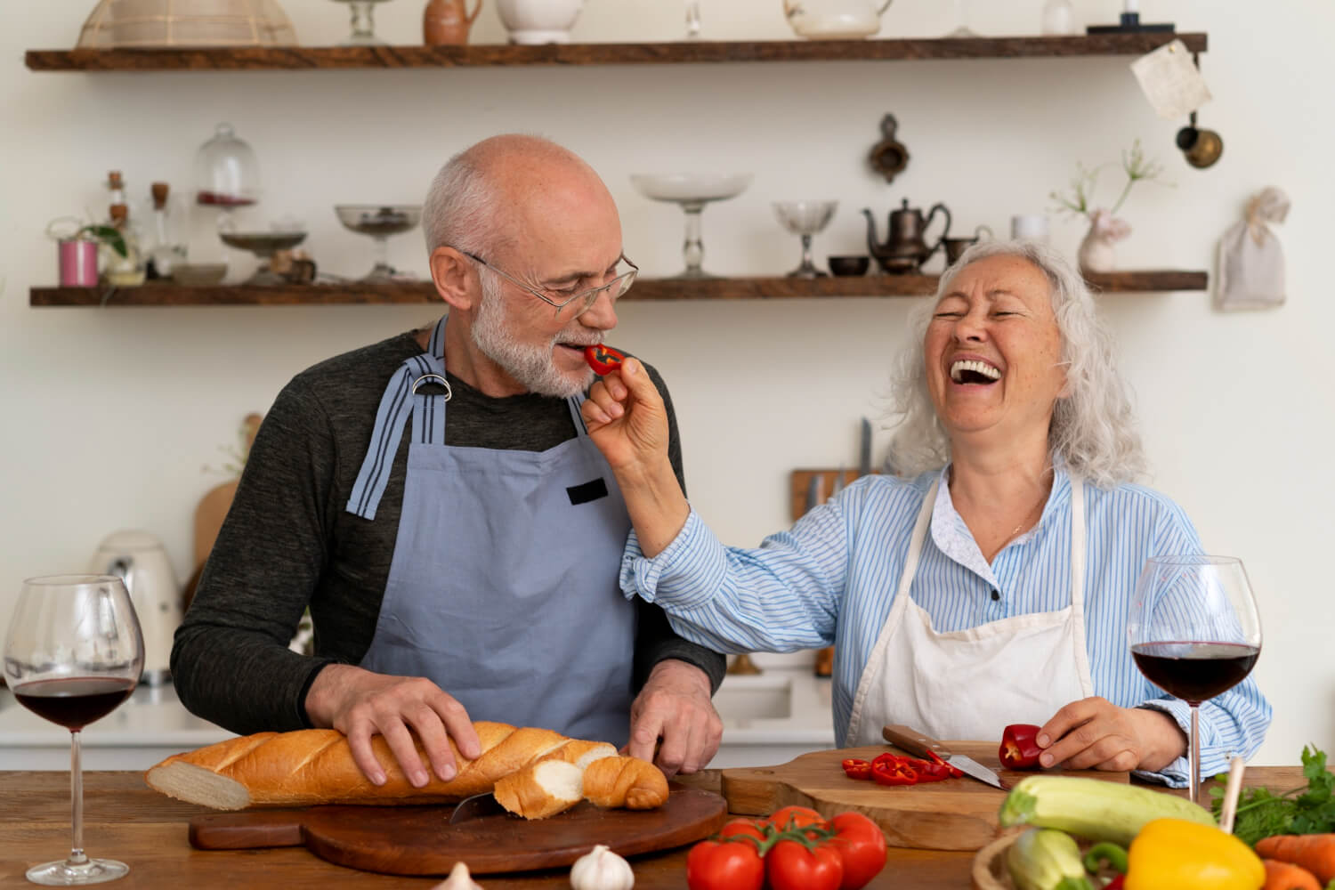 Casal idoso sorridente preparando uma refeição na cozinha, destacando a liberdade de mastigação com prótese protocolo em Aricanduva.