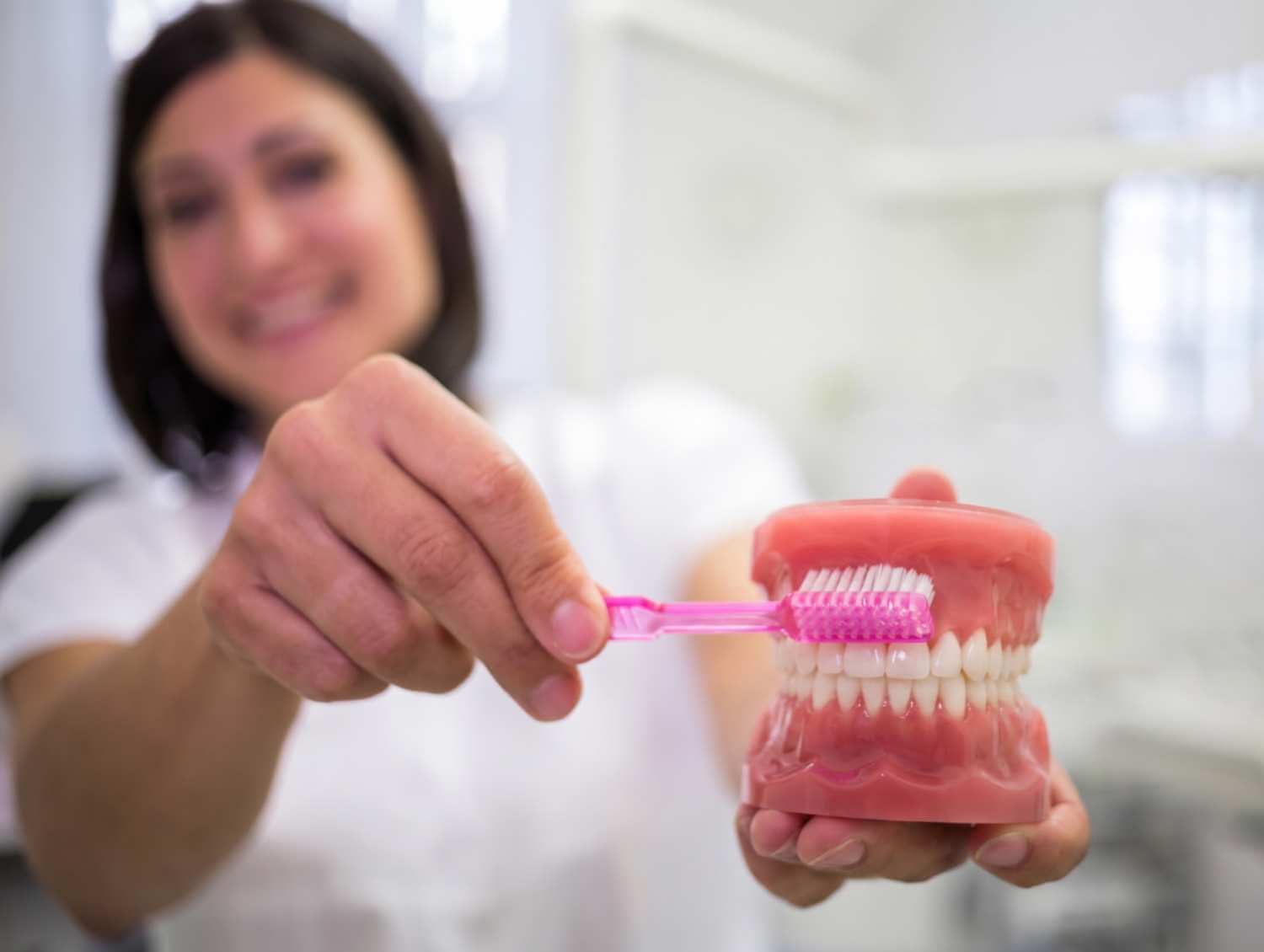 Dentista ensina como higienizar prótese protocolo com escova de dentes em modelo bucal na Myai Odontologia no Aricanduva.